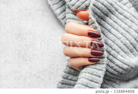 Elegant hand with deep red manicure holding a cozy gray sweater against a textured background  118864808