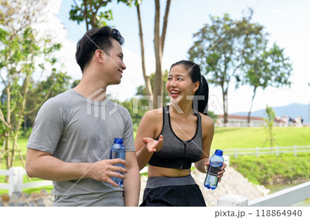 A happy, healthy Asian couple enjoys chatting while resting together after jogging in a public park. 118864940