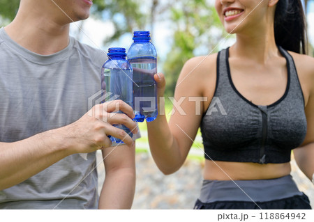 A cropped image of a healthy Asian couple in sportswear drinking water after jogging together. 118864942