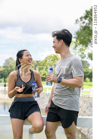 A happy, healthy Asian couple enjoys chatting while resting together after jogging in a public park. 118864952