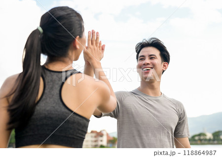 An active, happy Asian couple in sportswear gives each other a high five after running together. An active, happy Asian couple in sportswear gives each other a high five after running together. 118864987