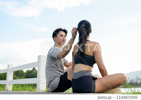 A lovely, sporty Asian couple in sportswear sits by the lake, resting after a morning run together. 118865000