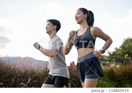 An active, sporty Asian couple in sportswear is enjoying a run together in a park in the morning. 118865014