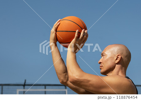 Basketball player or man tries to throw ball into basketball hoop on sports court. Game moment. Summer outdoors training. Basketball Throwing Technique. Basketball player or man tries to throw ball into basketball hoop on sports court. Game moment. Summer outdoors training. Basketball Throwing Technique. 118876454