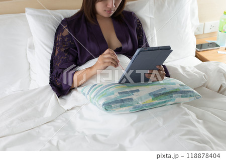 A woman works on her tablet at night, comfortably settled on the bed. 118878404