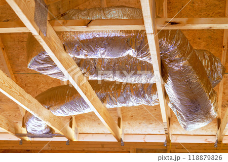 Installing ventilation HVAC pipes with silver insulation on roof ceiling during construction 118879826