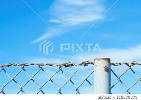 A rusty chain link fence against a bright blue sky with fluffy clouds on a sunny day outdoors A rusty chain link fence against a bright blue sky with fluffy clouds on a sunny day outdoors 118879879
