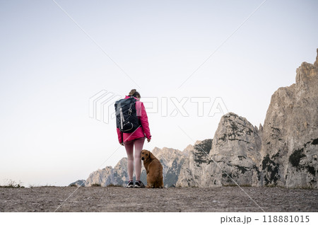 Female hiker in pink jacket standing on top of a mountain with her dog Female hiker in pink jacket standing on top of a mountain with her dog 118881015
