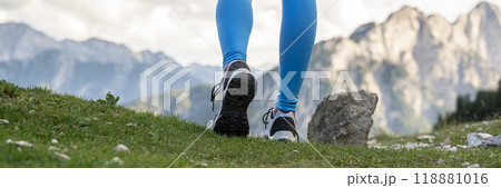 Low angle view of female legs in hiking shoes walking on a green mountain  trail 118881016