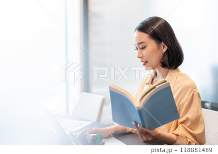参考書を片手にパソコン作業をする女性 118881489