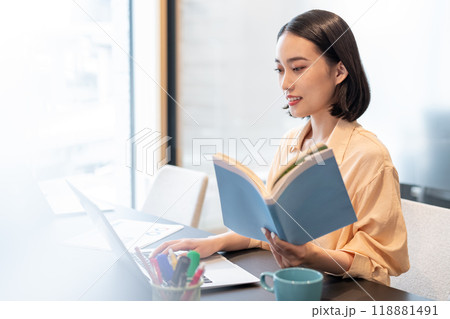 参考書を片手にパソコン作業をする女性 118881491