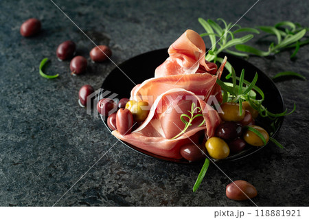 Italian prosciutto crudo with olives and rosemary on a black stone table. Italian prosciutto crudo with olives and rosemary on a black stone table. 118881921