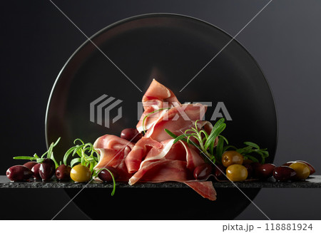 Prosciutto with olives and rosemary on a black background. Prosciutto with olives and rosemary on a black background. 118881924