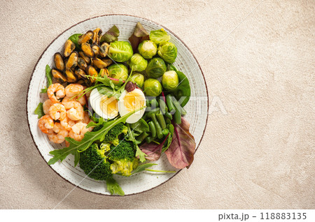 Shrimp and mussels cooked in coconut oil, served with greens, brussels sprouts, broccoli and eggs. Keto diet. 118883135