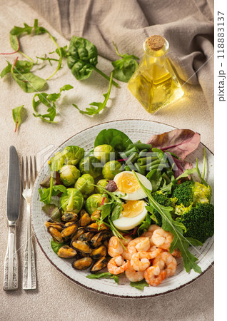 Shrimp and mussels cooked in coconut oil, served with greens, brussels sprouts, broccoli and eggs. Keto diet. 118883137