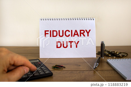 White note with inscription 'fiduciary duty' on beautiful wooden table, male hand on calculator, pen, paper clips, coins. Business concept. White background. White note with inscription 'fiduciary duty' on beautiful wooden table, male hand on calculator, pen, paper clips, coins. Business concept. White background. 118883219