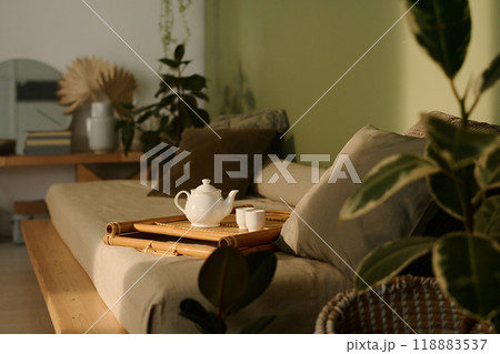 White ceramic teapot and cups on wooden tray on couch in wabi sabi living room interior White ceramic teapot and cups on wooden tray on couch in wabi sabi living room interior 118883537