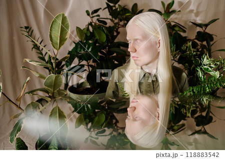 Young woman with albinism and her mirror image in studio decorated with green houseplants, conceptual portrait Young woman with albinism and her mirror image in studio decorated with green houseplants, conceptual portrait 118883542