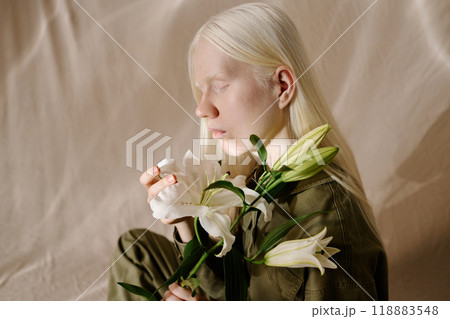 Side view medium closeup studio shot of young woman with albinism holding fresh white lily flowers 118883548