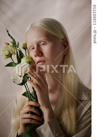 Vertical medium closeup studio portrait of young Caucasian woman with albinism posing for camera with white eustoma flowers Vertical medium closeup studio portrait of young Caucasian woman with albinism posing for camera with white eustoma flowers 118883558