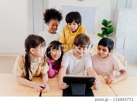 Diverse elementary students collaborate on digital tablet in modern classroom. Multicultural group engages in interactive learning, showcasing inclusive education and technological integration 118883772