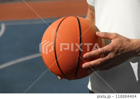 Basketball player, man holding orange ball on sports court. Sports goals competition game, champion outdoor workout. Close up. Copy space Basketball player, man holding orange ball on sports court. Sports goals competition game, champion outdoor workout. Close up. Copy space 118884404