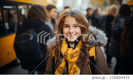 Smiling caucasian schoolgirl with a backpack is standing at the door of a school bus with her friends. Elementary school. Concept back to school. 118884435