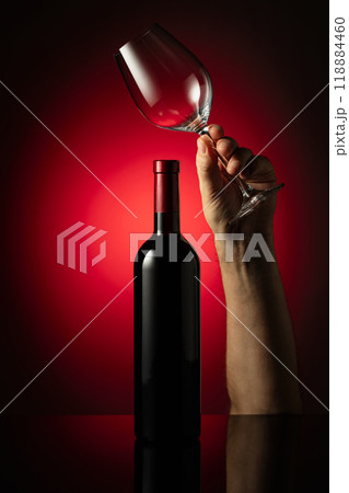 Unopened bottle of red wine and hand with wine glass. 118884460