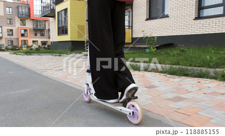 Schoolgirl rides her scooter down a quiet street, her backpack on as the morning sun lights her path Schoolgirl rides her scooter down a quiet street, her backpack on as the morning sun lights her path 118885155