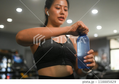 Tired young fitness woman taking a break from her workout and drinking water Tired young fitness woman taking a break from her workout and drinking water 118885829