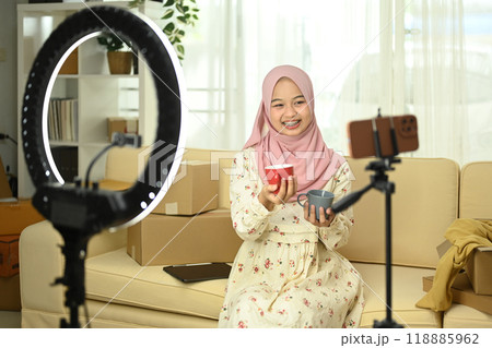 Happy young Muslim woman live streaming and presenting ceramics products to her audience. E-commerce concept Happy young Muslim woman live streaming and presenting ceramics products to her audience. E-commerce concept 118885962