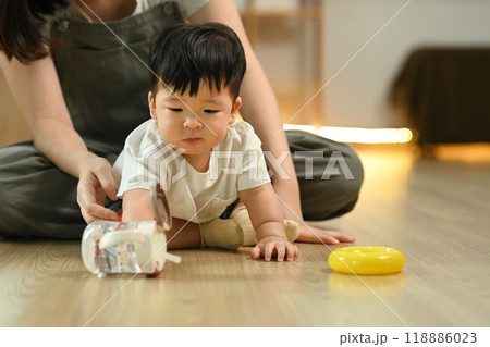 Cute baby boy learning to crawl with supportive mother closely watching from behind. Childhood and development concept 118886023