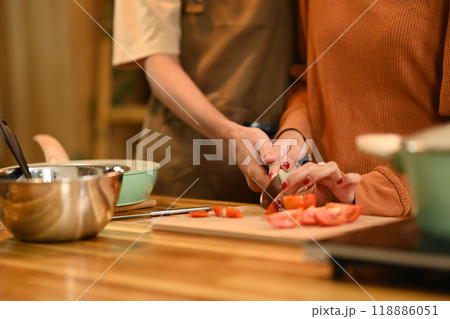 Young couple cutting tomatoes on a wooden cutting board, preparing spaghetti bolognese in kitchen Young couple cutting tomatoes on a wooden cutting board, preparing spaghetti bolognese in kitchen 118886051
