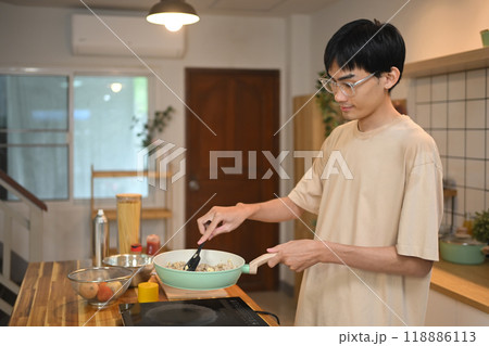 Young asian man using a spatula to stir and cook the ingredients in frying pan on an induction stove Young asian man using a spatula to stir and cook the ingredients in frying pan on an induction stove 118886113