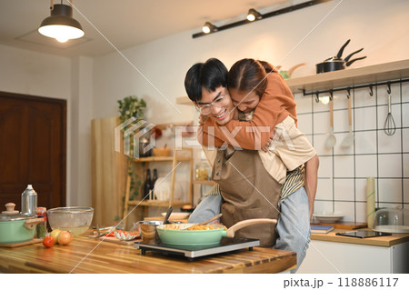 Joyful young couple wearing aprons cooking in a cozy kitchen. Relationships, cooking and happy domestic life Joyful young couple wearing aprons cooking in a cozy kitchen. Relationships, cooking and happy domestic life 118886117