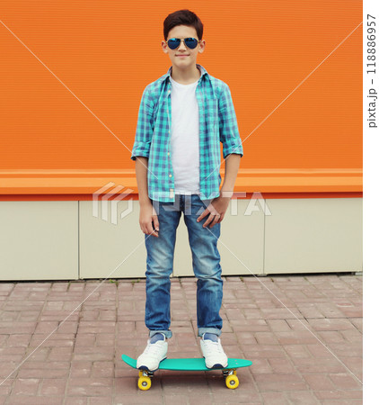 Modern teenage kid boy with skateboard in casual clothes standing on city street Modern teenage kid boy with skateboard in casual clothes standing on city street 118886957