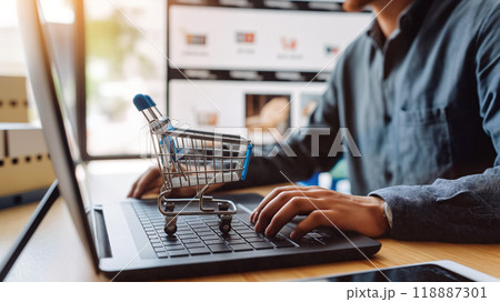 Person working on a laptop with a miniature shopping trolley placed on the keyboard during online shopping 118887301