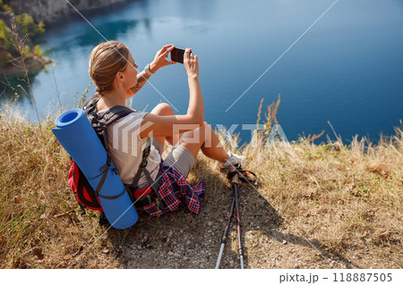 A Hiker Capturing a Scenic View with a Smartphone Near a Calm and Serene Lake Setting 118887505