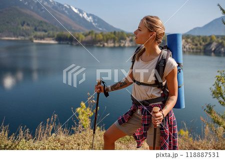 A woman hiker with a backpack enjoys scenic views near a lake and stunning mountains 118887531
