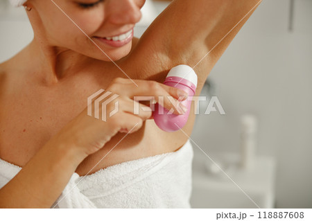 A woman applies deodorant in her bathroom, showing her confident daily beauty routine 118887608