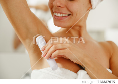 In a stylish bathroom, a woman applies deodorant to stay fresh and confident all day 118887615