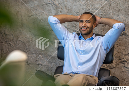 Smiling businessman sitting in chair with raised arms in office 118887867