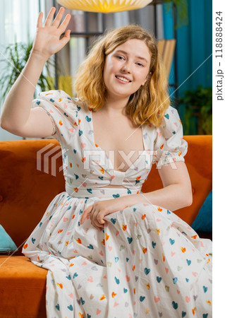 Pretty woman smiling friendly at camera, waving hands gesturing hello, hi, greeting at home on sofa Pretty woman smiling friendly at camera, waving hands gesturing hello, hi, greeting at home on sofa 118888424