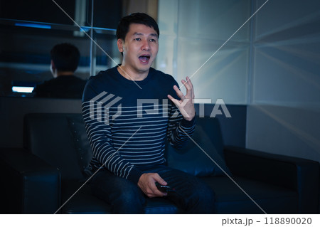 shocked and scared man is watching horror movie TV on sofa at night shocked and scared man is watching horror movie TV on sofa at night 118890020