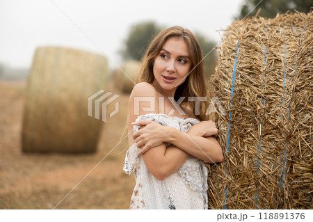 Sexy woman in white dress having picnic standing by hay bales in farm field Sexy woman in white dress having picnic standing by hay bales in farm field 118891376