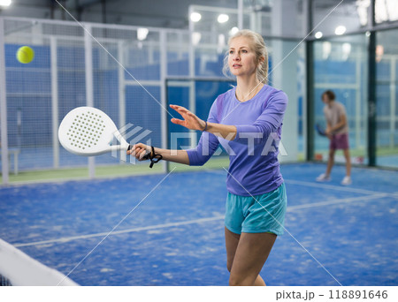 Sporty woman padel player hitting ball with a racket on hard court Sporty woman padel player hitting ball with a racket on hard court 118891646
