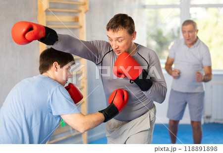 Man getting powerful blow to body during boxing sparring with young opponent Man getting powerful blow to body during boxing sparring with young opponent 118891898