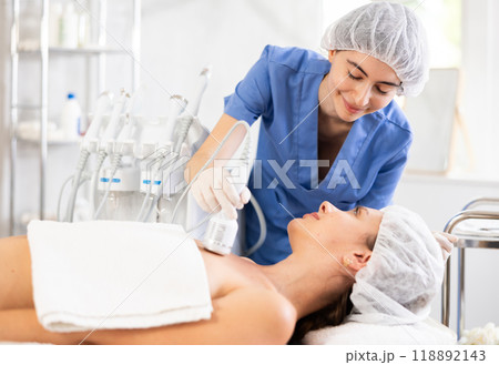 Female cosmetologist performing procedure on decollete area to woman using cooling attachment 118892143