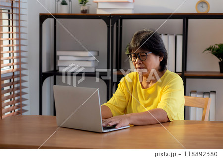 Elderly woman using laptop with office desk at home, senior woman typing on laptop. 118892380