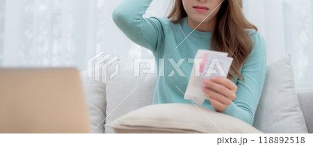 Young asian woman wearing glasses sitting on sofa worried with bills about financial and stress. 118892518